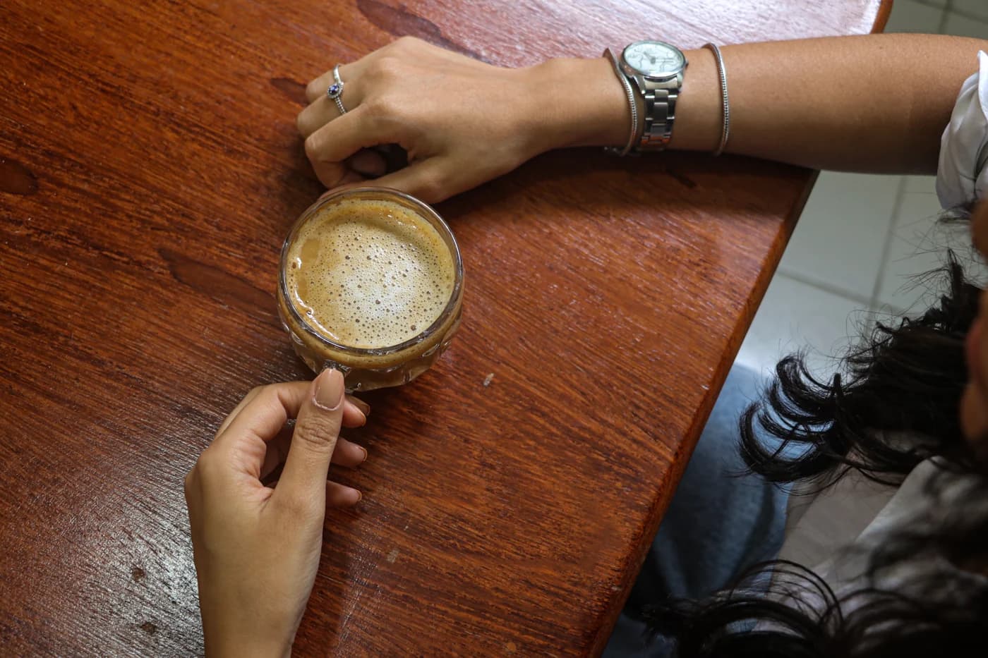 Mãos de Isabella segurando uma xícara de café sobre uma mesa de madeira.